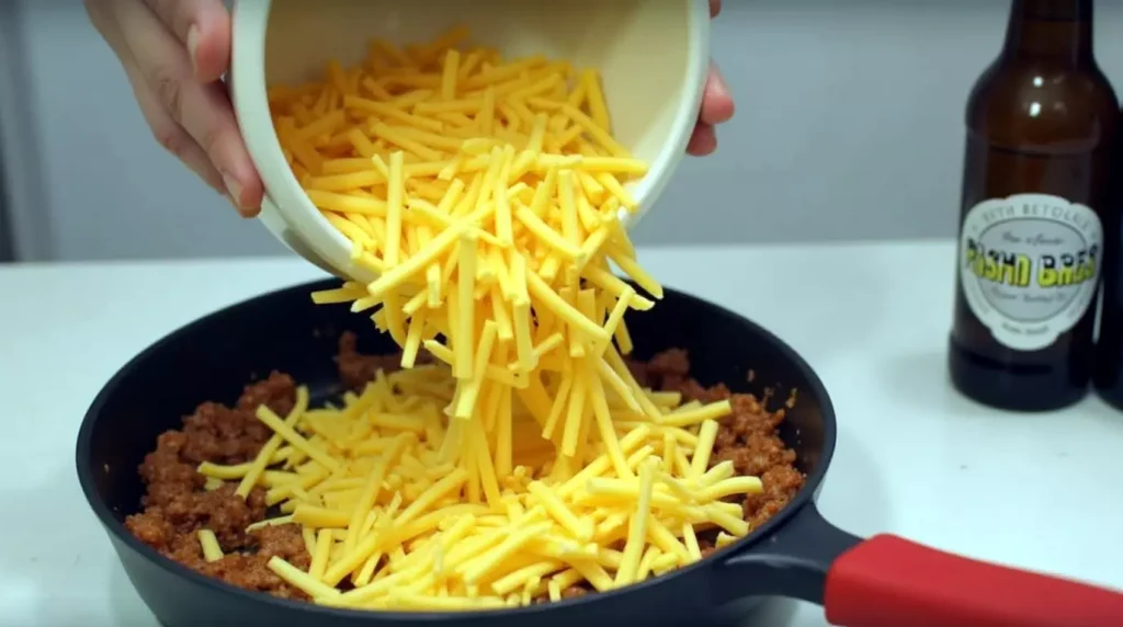 Shredded cheese and beer being added to a skillet of cooked sausage